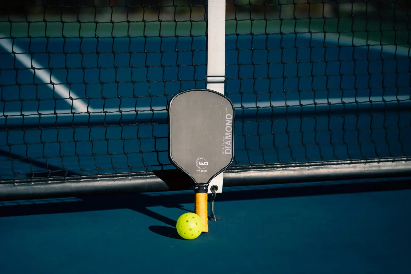 Black pickleball racquet standing upright agains a black pickleball net on a court