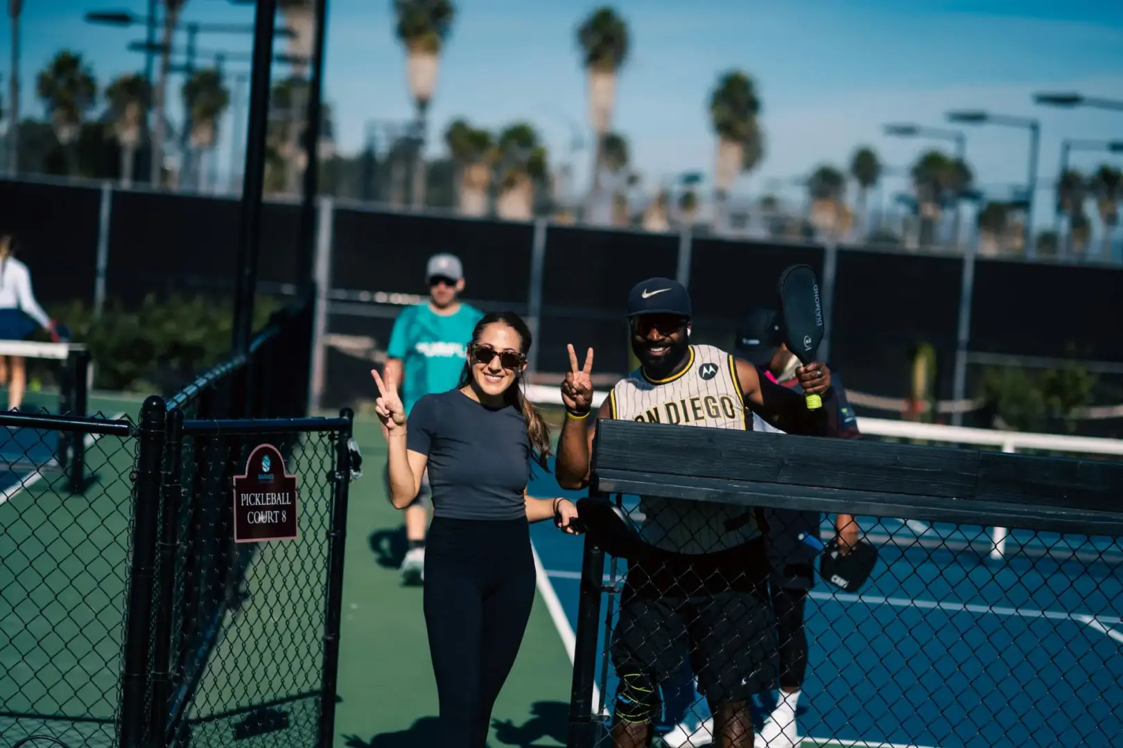 two pickleball players holding up peace signs with their fingers on pickleball court