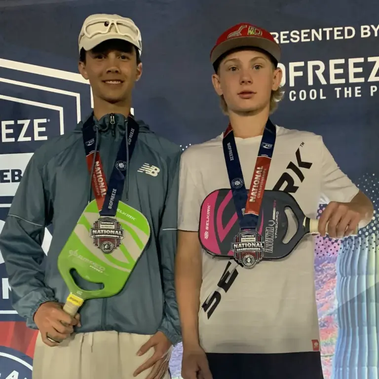 two young boy pickleball players showing medals in front of their pickleball paddles
