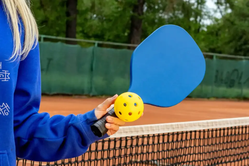 young girl holding a blue pickleball raquet and yellow pickleball